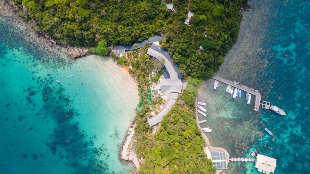 Aerial view of a jungle island in the An Thoi archipelago with a white-sand beach, coral reefs and tour boats at the pier
